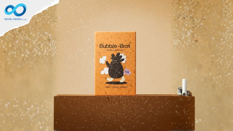 กล่อง Bubble-Brot สีส้มรุ่น dark ตั้งบนแท่นสีน้ำตาล มีละอองน้ำในฉาก