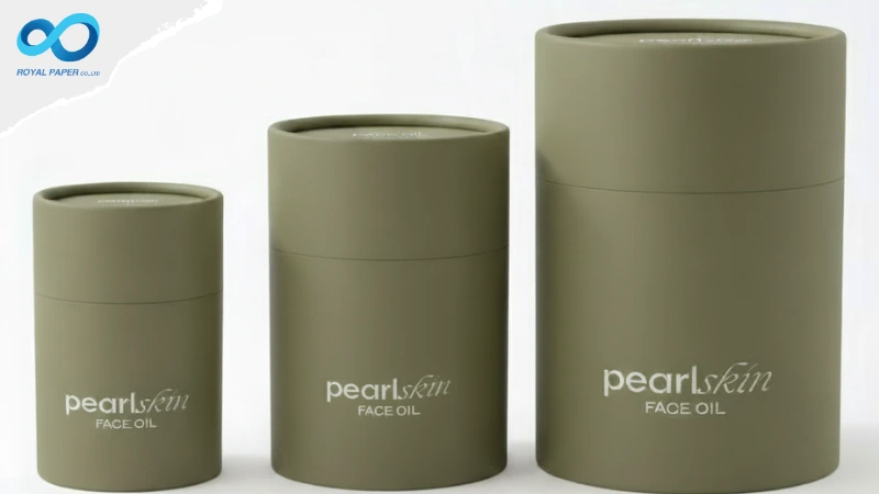 กล่องทรงกระบอกสีเขียวโอลิฟ 3 ขนาด วางเรียงจากเล็กไปใหญ่ พิมพ์ข้อความ “pearlskin FACE OIL” ที่ตัวกล่อง